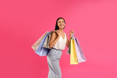 Beautiful young woman with paper shopping bags on pink background