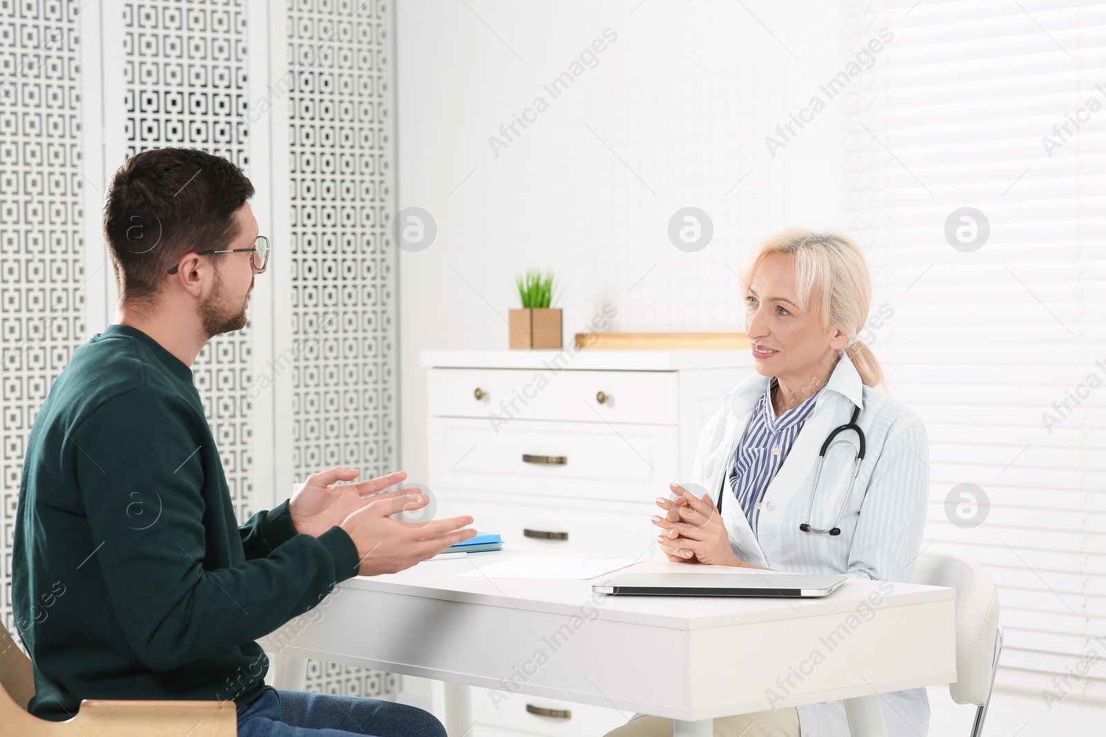 Photo of Doctor consulting patient at white table in clinic