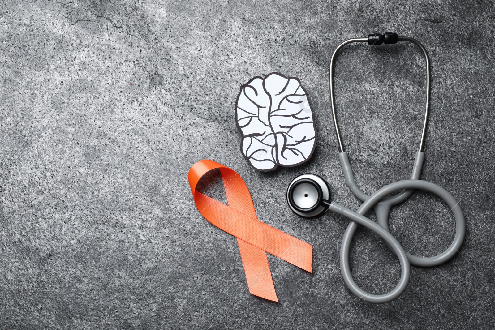 Photo of Orange ribbon, stethoscope and paper brain cutout on grey table, flat lay with space for text. Multiple sclerosis awareness