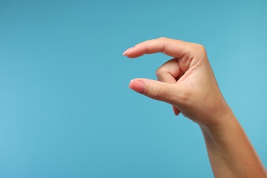 Photo of Woman holding something in fingers on light blue background, closeup. Space for text