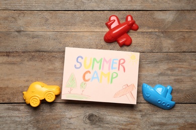 Photo of Card with text SUMMER CAMP, drawings and different sand molds on wooden table, flat lay