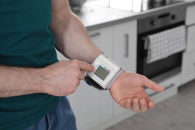 Photo of Young man checking pulse with digital medical device indoors, closeup