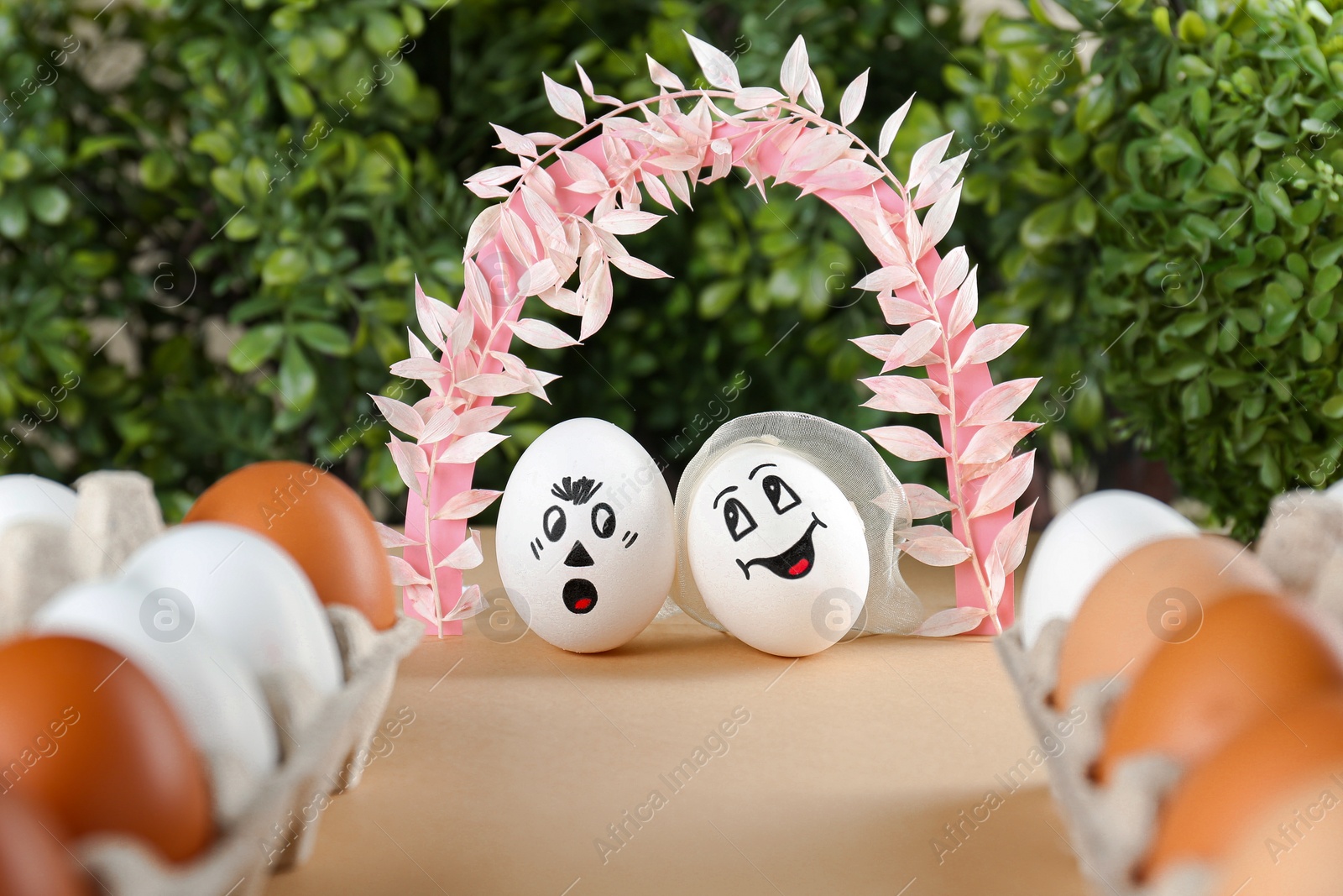 Photo of Eggs with drawn faces as bride and groom under decorative arch on table during wedding