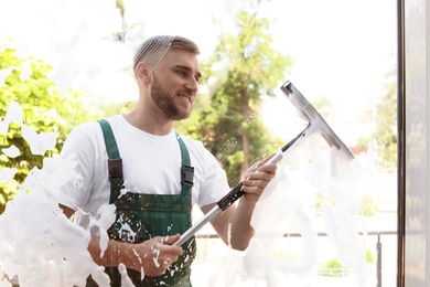 Male cleaner wiping window glass with squeegee from outside