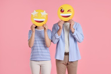 People covering faces with emoticons on pink background