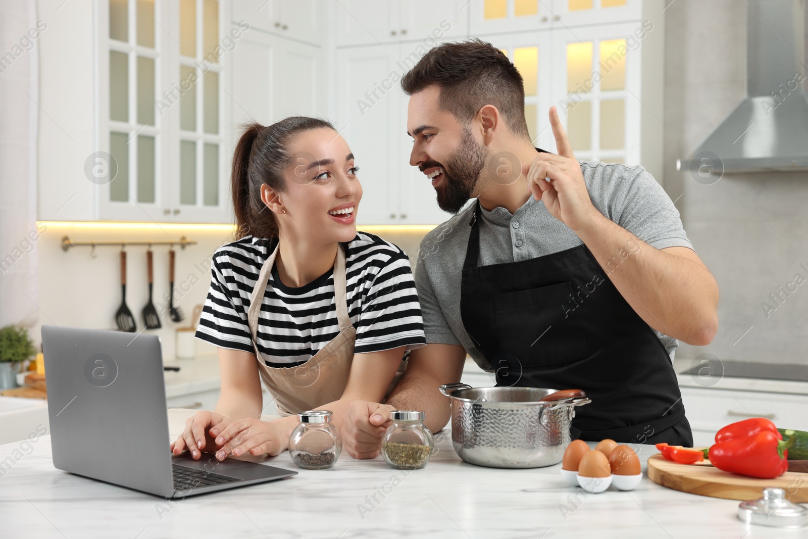 Photo of Happy lovely couple using laptop while cooking in kitchen