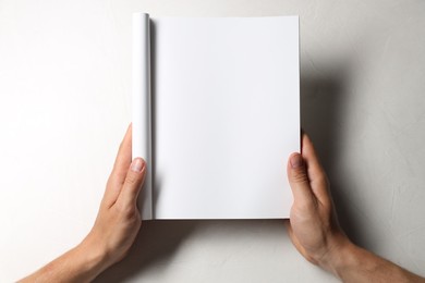 Photo of Man holding blank notebook at white table, top view. Mockup for design