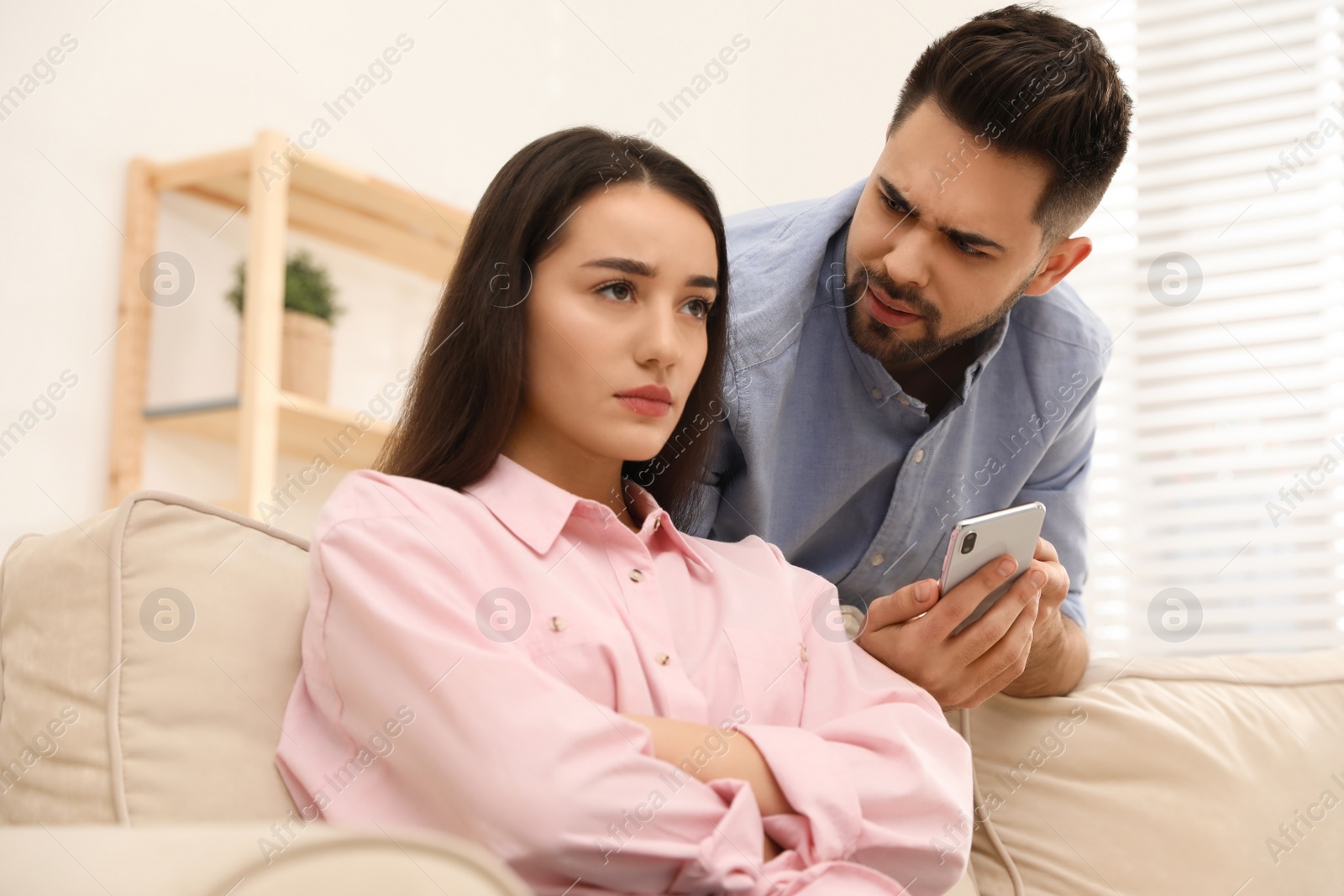 Photo of Young couple arguing about smartphone at home. Problems in relationship