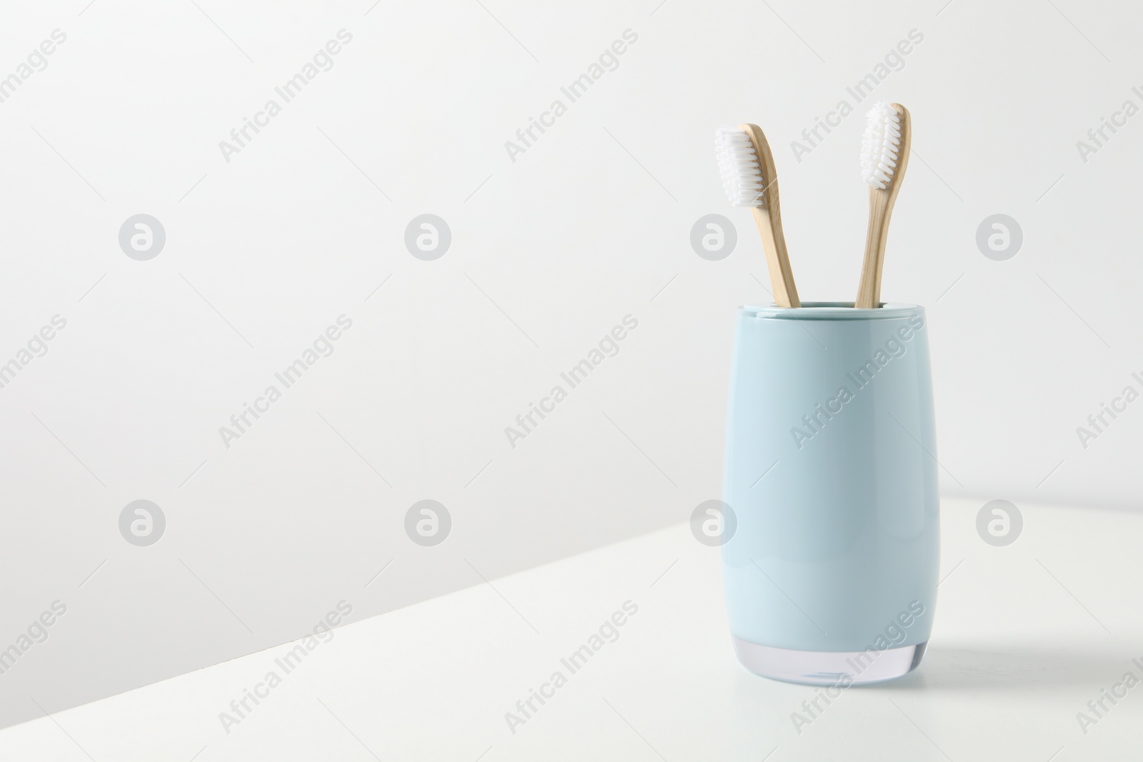 Photo of Bamboo toothbrushes in holder on white table, space for text