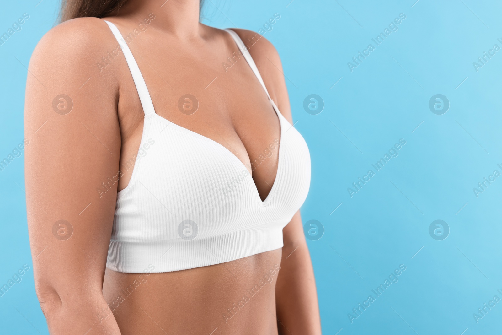 Photo of Woman with beautiful breast on light blue background, closeup. Space for text