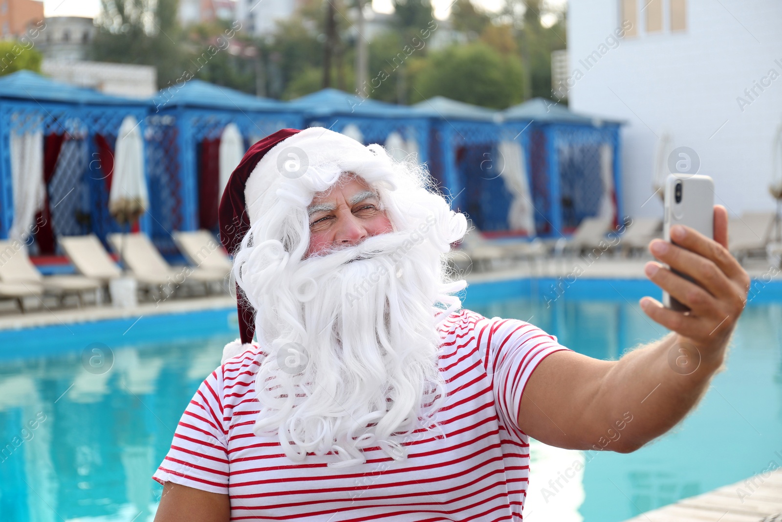 Photo of Authentic Santa Claus taking selfie near swimming pool outdoors