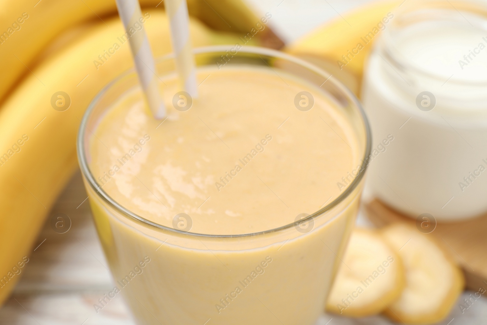 Photo of Glass of tasty banana smoothie with straws and ingredients on table, closeup