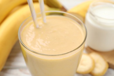 Glass of tasty banana smoothie with straws and ingredients on table, closeup