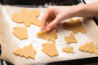 Photo of Woman putting raw Christmas cookies on baking tray at table, closeup