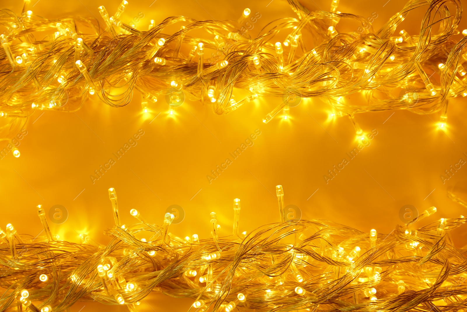 Photo of Glowing Christmas lights on yellow background, top view. Space for text