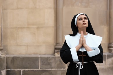 Photo of Young nun with hands clasped together praying outdoors, space for text