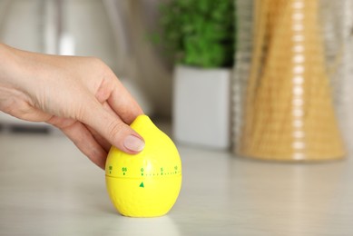 Photo of Woman winding up kitchen timer in shape of lemon at white table indoors, closeup. Space for text