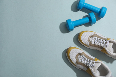 Photo of Dumbbells, sneakers and space for text on light grey background, flat lay. Physical fitness