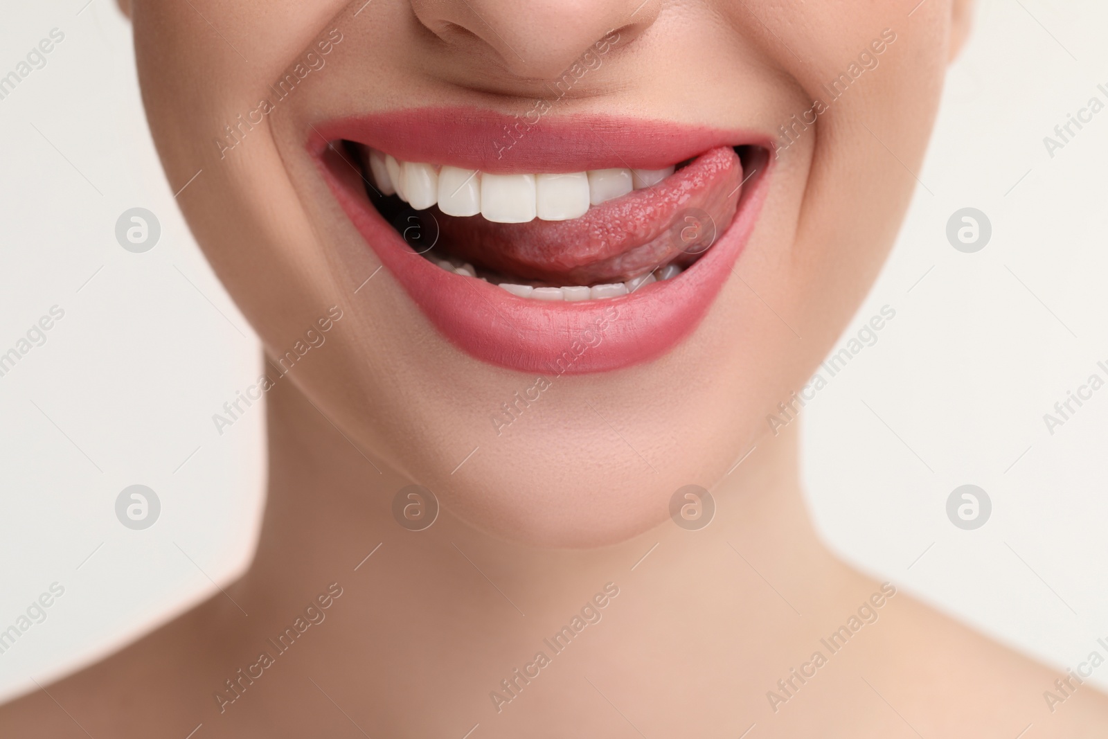 Photo of Young woman licking her teeth on white background, closeup