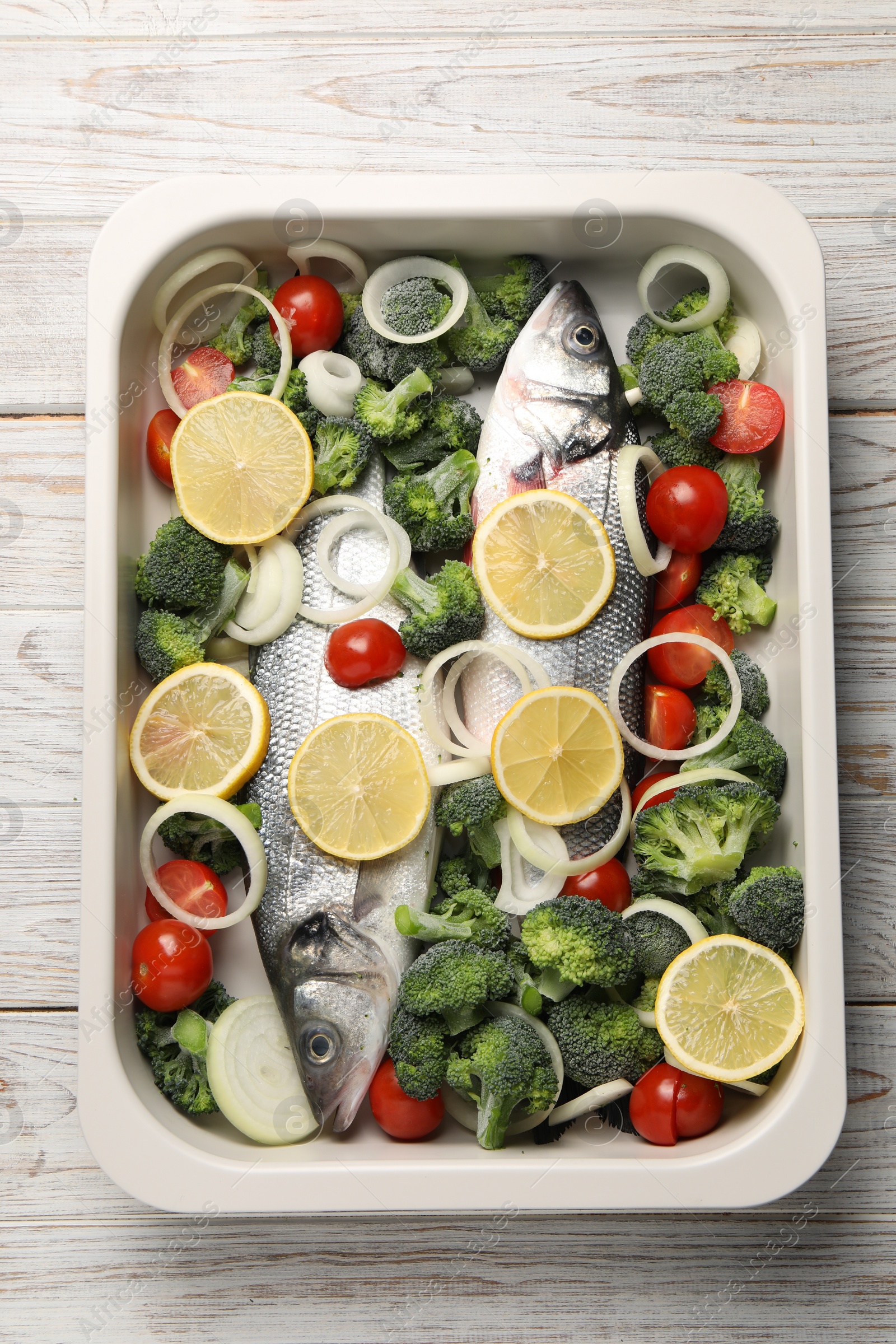 Photo of Raw fish with vegetables and lemon in baking dish on wooden table, top view