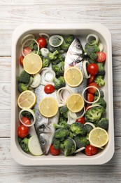 Raw fish with vegetables and lemon in baking dish on wooden table, top view