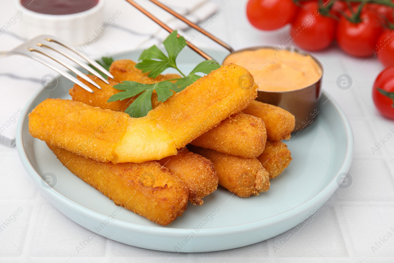 Photo of Tasty fried mozzarella sticks served with sauce and parsley on white tiled table