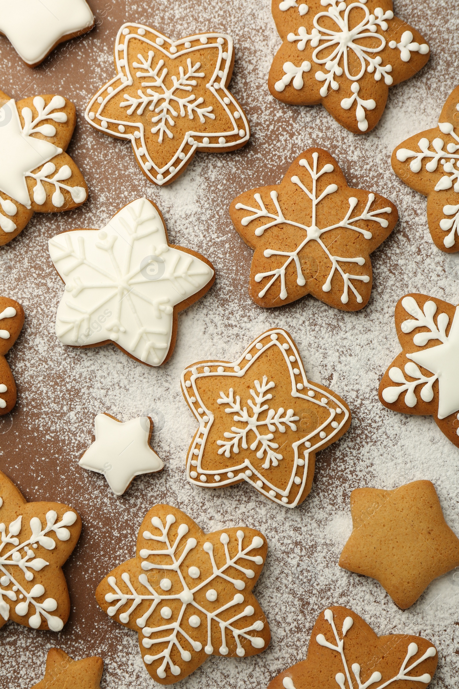 Photo of Tasty Christmas cookies with icing and powdered sugar on brown background, flat lay