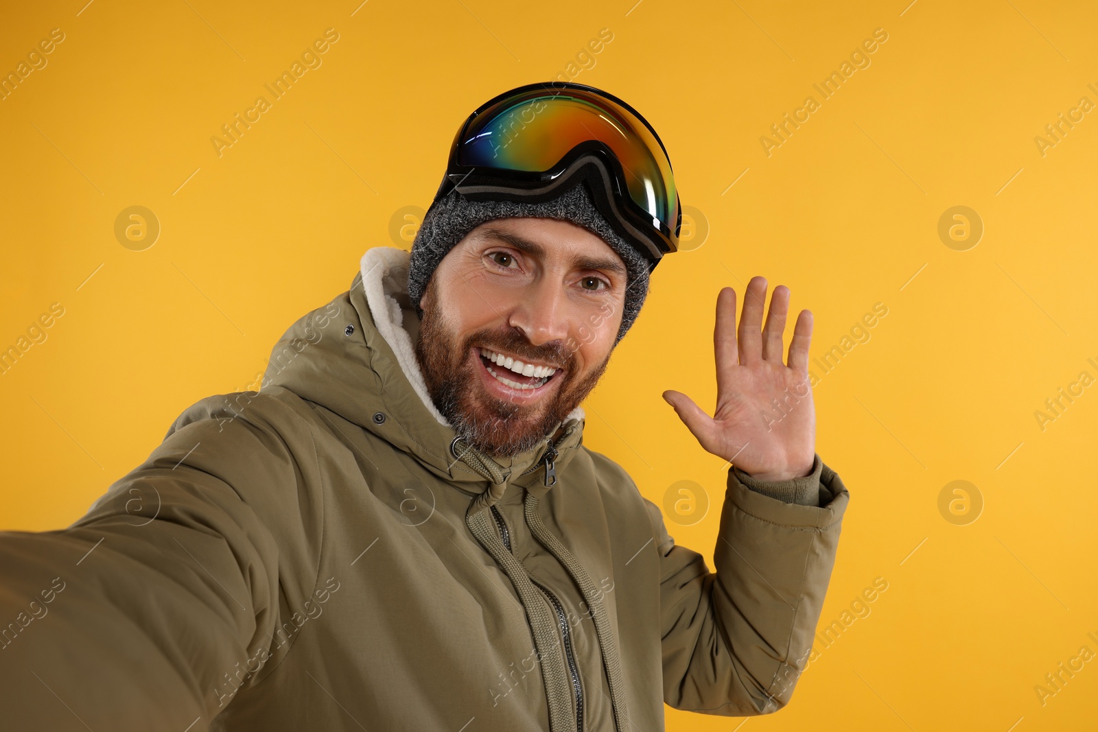 Photo of Winter sports. Happy man in ski suit and goggles taking selfie on orange background, space for text