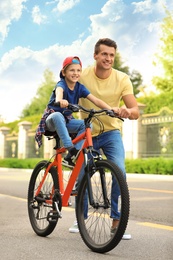 Photo of Dad teaching son to ride bicycle outdoors