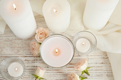 Flat lay composition with burning aromatic candles and roses on wooden table