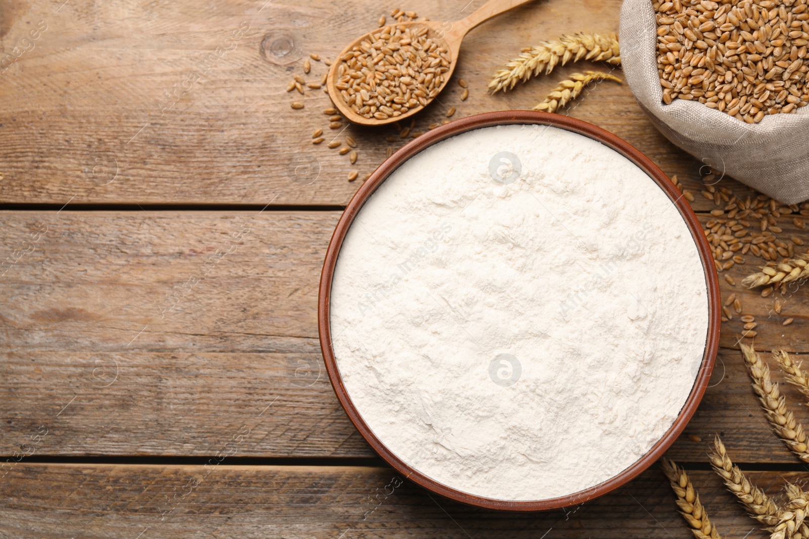 Photo of Wheat flour in bowl, spikes and grains on wooden table, flat lay. Space for text