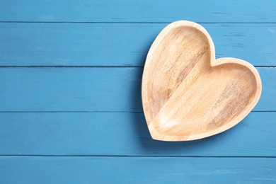 Photo of Empty heart shaped wooden plate on blue table, top view. Space for text