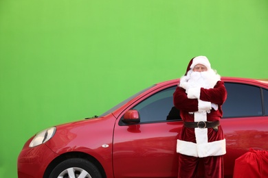 Authentic Santa Claus with red bag near car against green background
