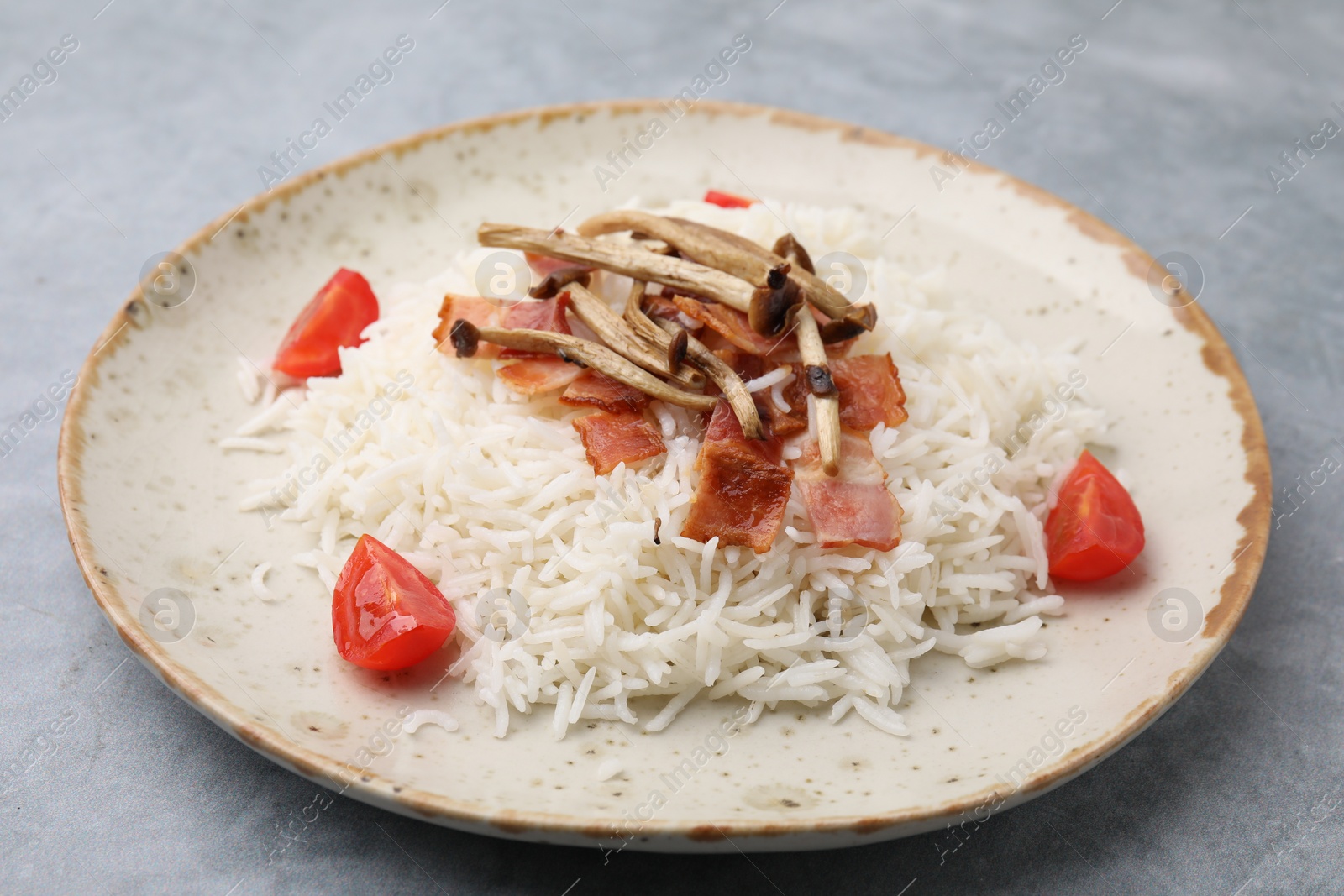 Photo of Delicious rice with bacon, mushrooms and tomatoes on gray table, closeup