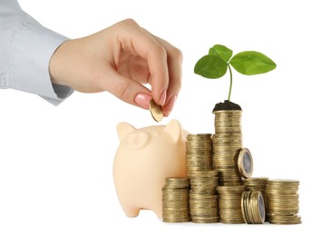 Photo of Woman adding cash into piggy bank near stacked coins with green sprout on white background, closeup