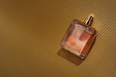 Photo of Luxury women's perfume. Sunlit glass bottle on golden surface, top view. Space for text