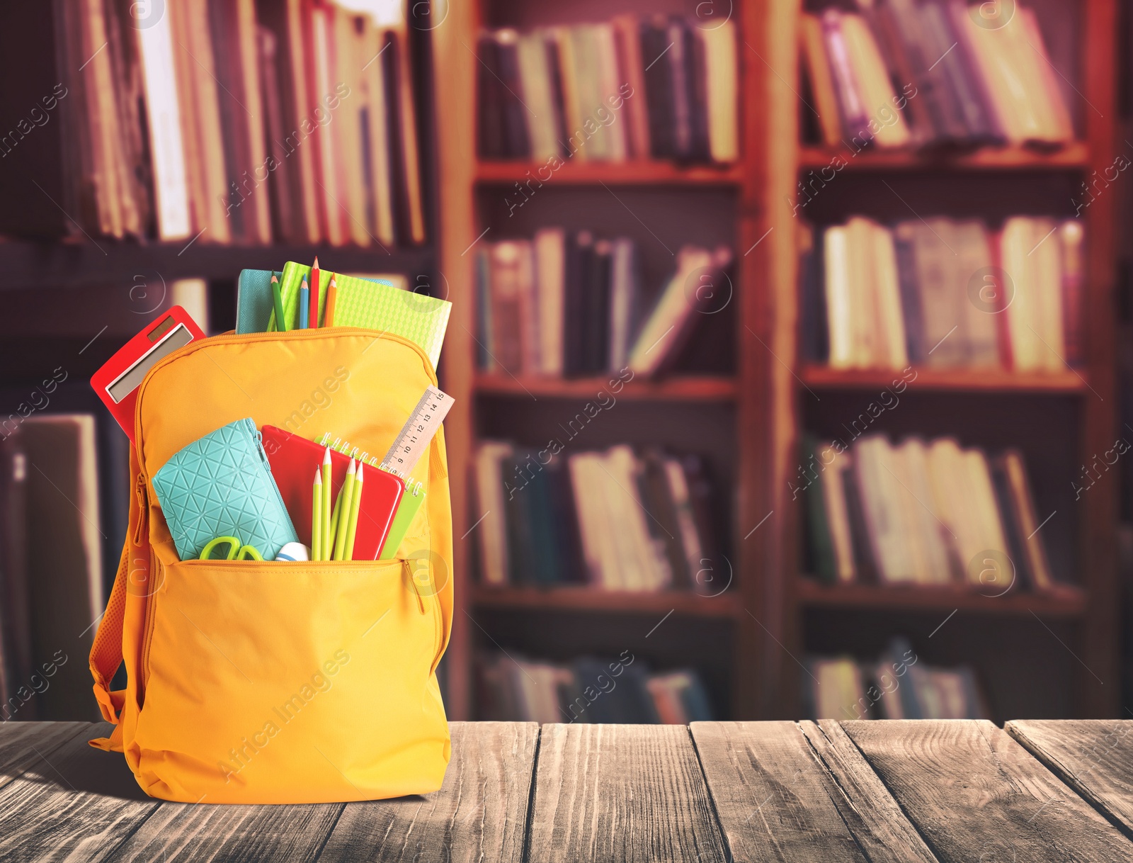 Image of Backpack with school stationery on wooden table in library, space for text