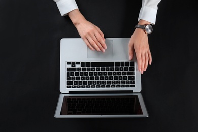 Young woman using laptop on black background, top view