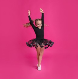 Photo of Cute little girl in black dress dancing on pink background