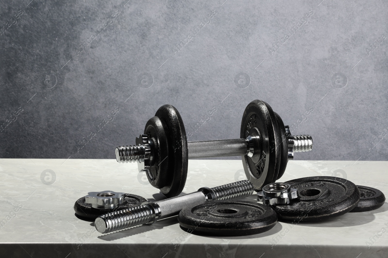 Photo of Barbell and parts of one on light table against grey background. Space for text
