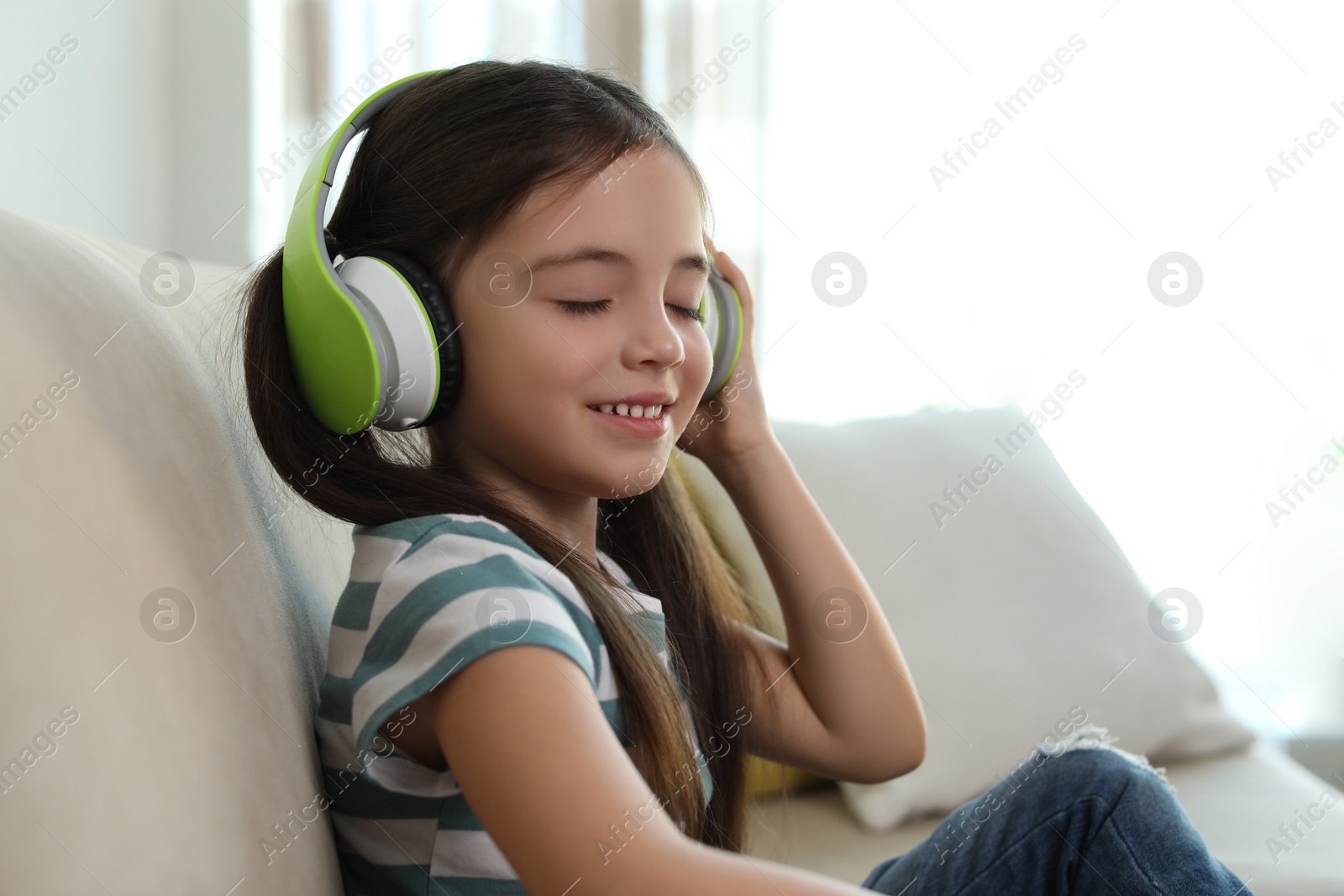 Photo of Cute little girl with headphones listening to audiobook at home