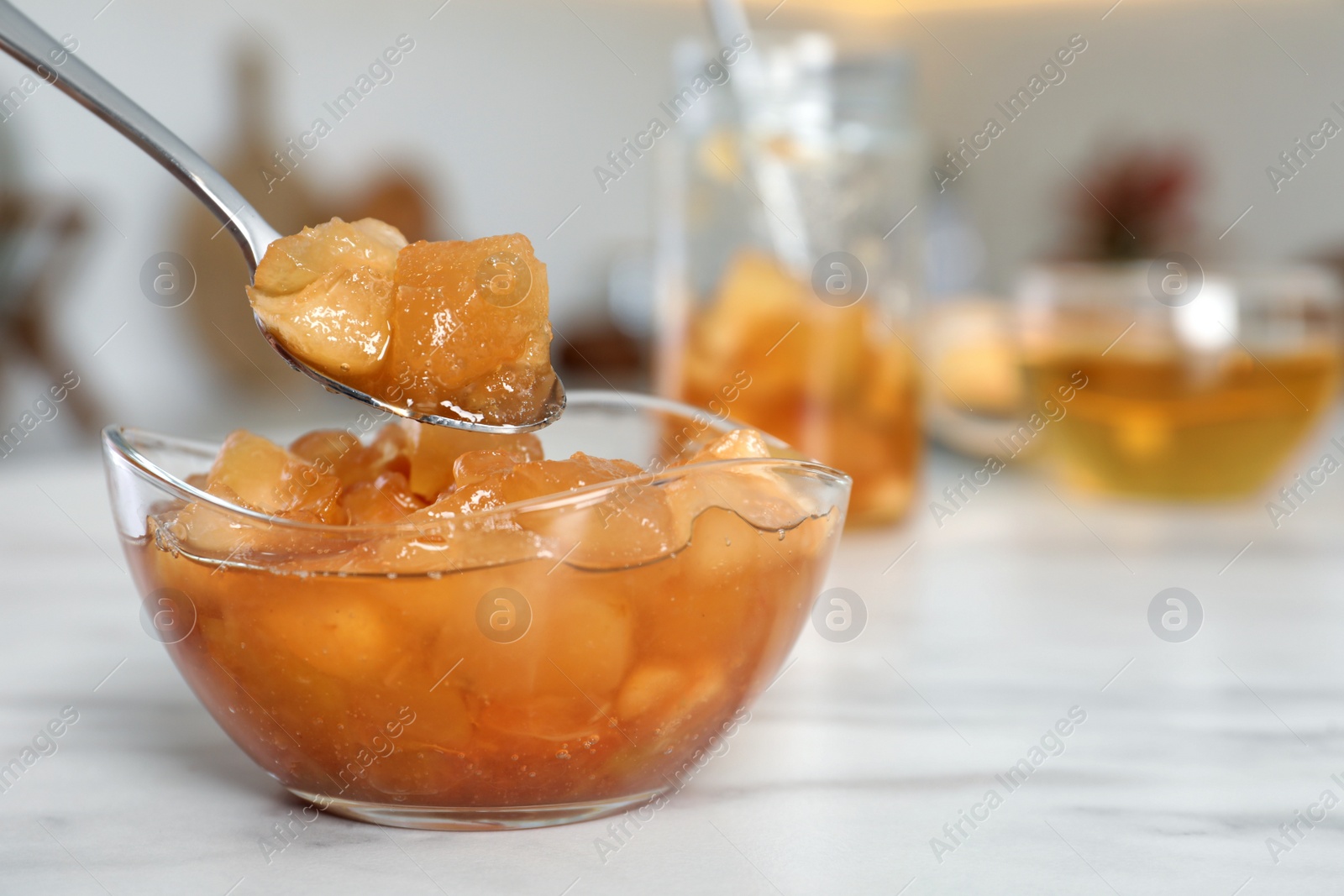 Photo of Spoon with delicious apple jam over bowl on white table, closeup