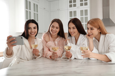 Photo of Beautiful young ladies with wine taking selfie in kitchen at pamper party. Women's Day