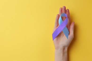 World Arthritis Day. Woman with blue and purple awareness ribbon on yellow background, top view. Space for text