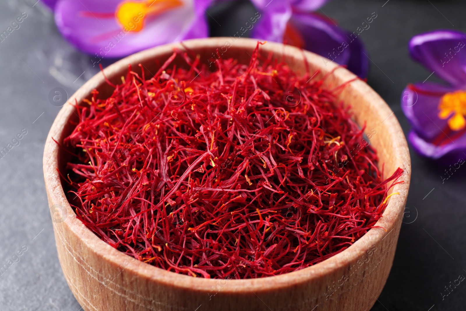 Photo of Dried saffron in bowl and crocus flowers on table, closeup