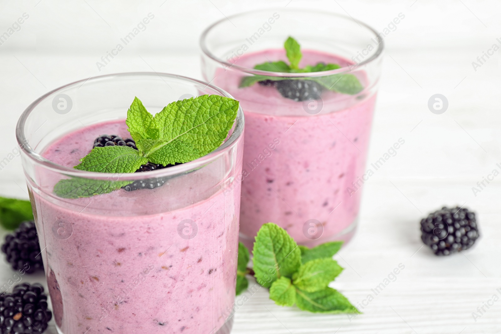 Photo of Delicious blackberry smoothie in glasses on white table, closeup