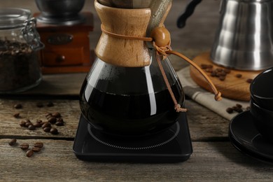 Photo of Glass chemex coffeemaker with coffee and beans on wooden table, closeup