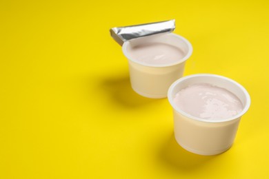 Photo of Plastic cups with tasty yogurt on yellow background, space for text