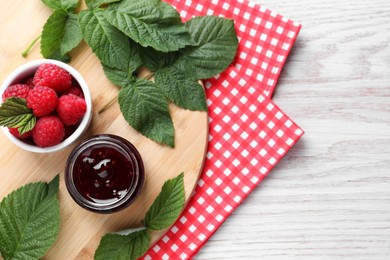 Jar of delicious raspberry jam, fresh berries and green leaves on white wooden table, top view. Space for text