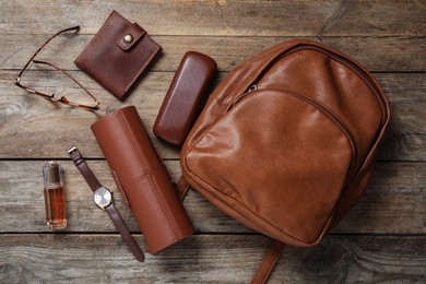 Photo of Stylish urban backpack and different items on wooden table, flat lay